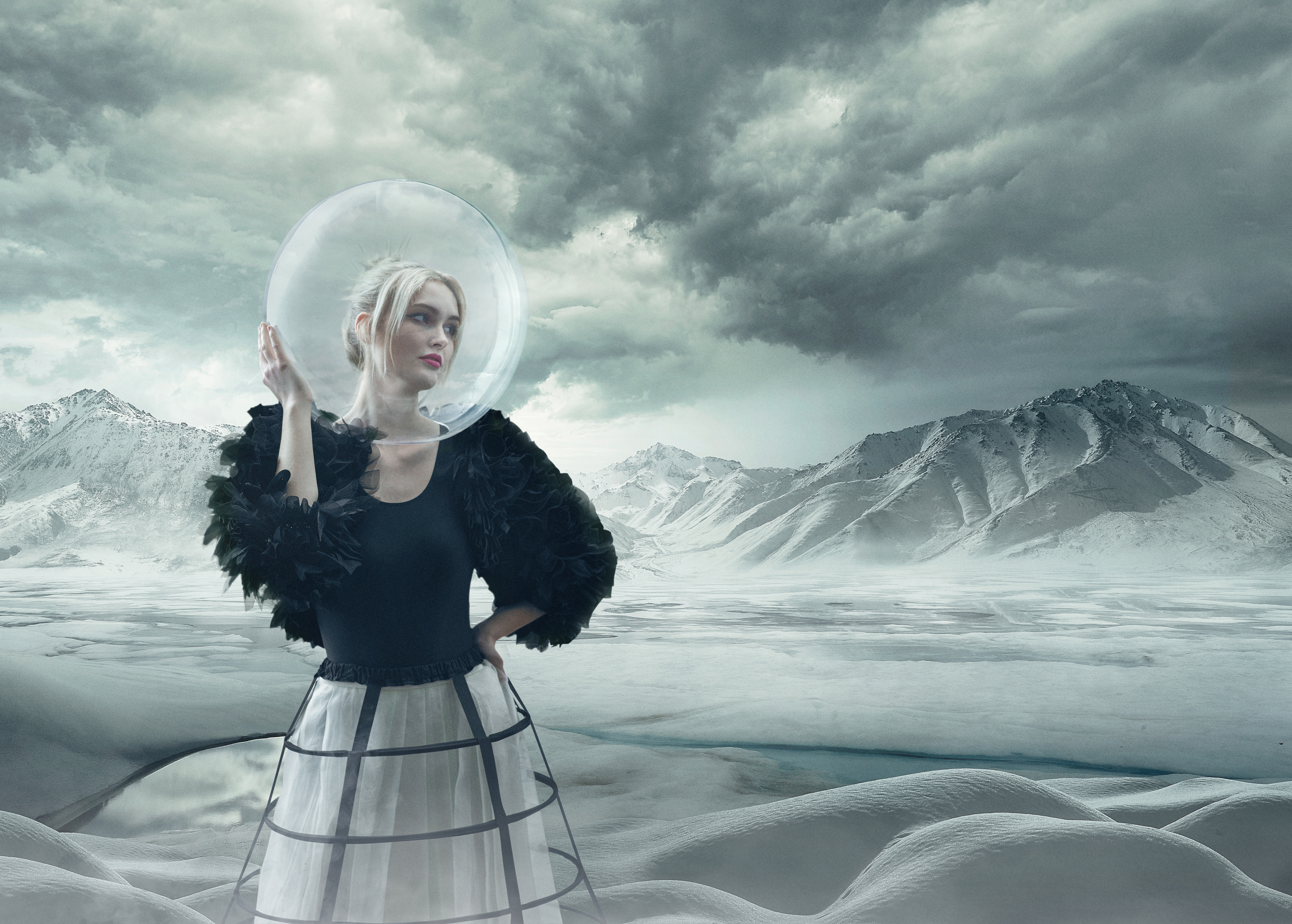 Fashionable woman with a clear dome over her head posing in a surreal, icy landscape with mountains, cloudy skies, and cool tones.