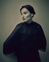 Portrait of a woman wearing a black sheer pleated blouse with her dark hair styled in braided crown by Jeff Sciortino.