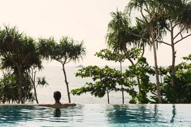 Woman in an outdoor infinity pool looking out toward the ocean surrounded by tropical palm trees in Brisbane.