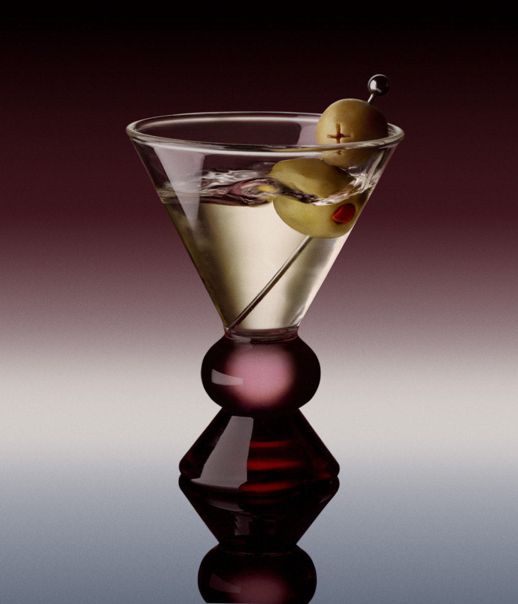 Martini cocktail in glass with olive garnish on a dark gradient background, reflecting on the surface below in a studio setting.