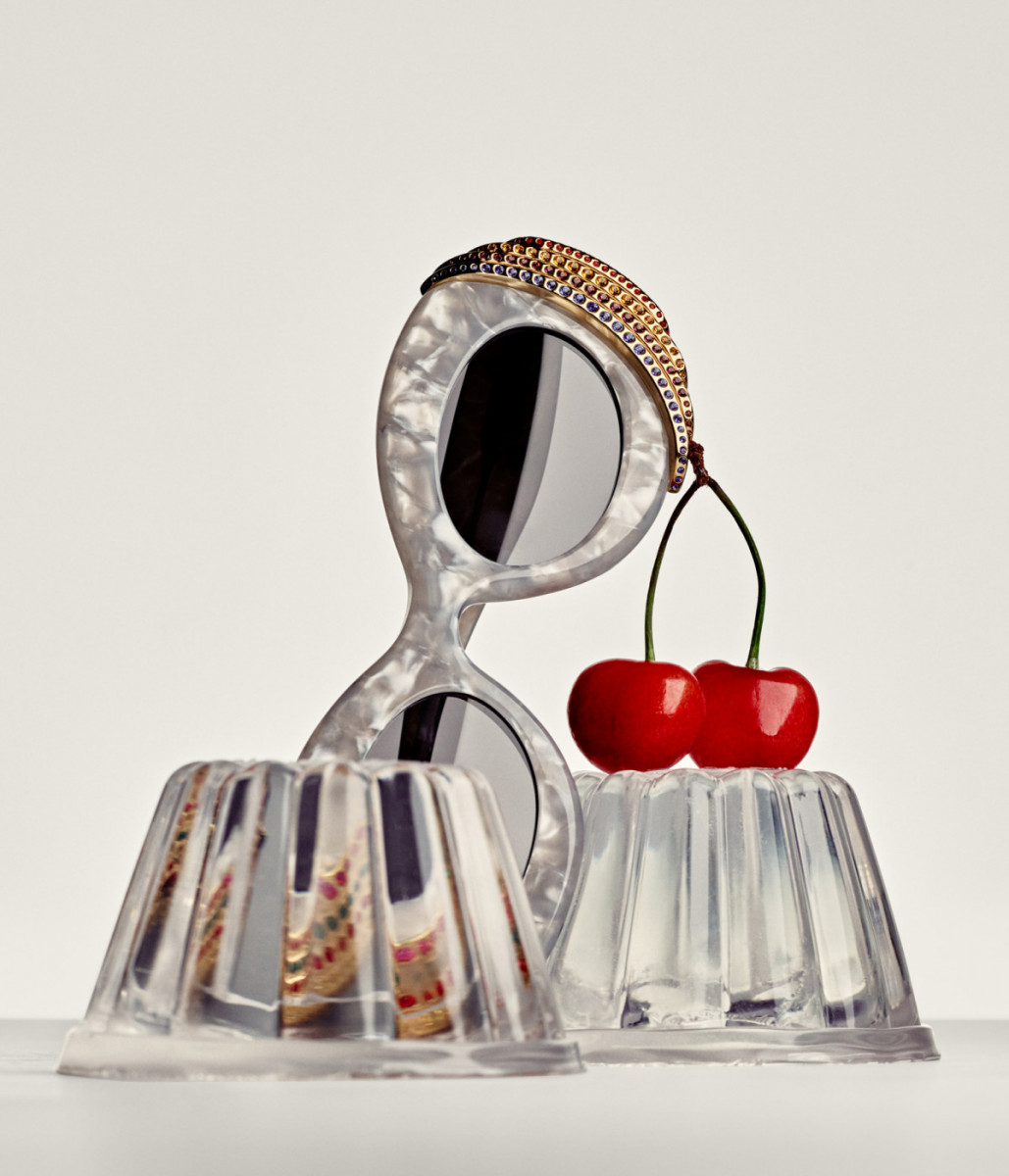 Still life of sunglasses adorned with cherries, perched on jello cups, creating a whimsical and visually striking composition on a light surface.