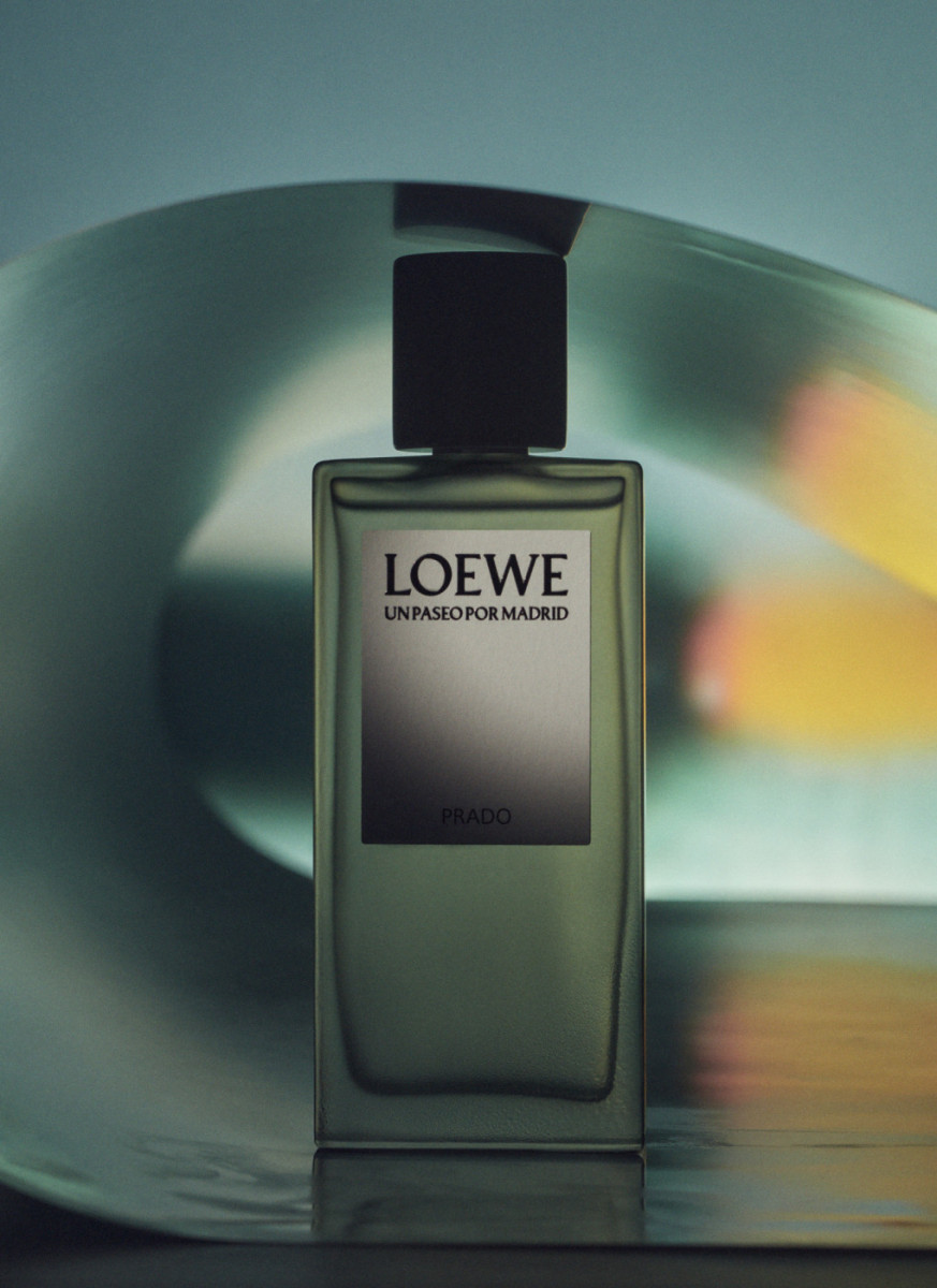 Loewe 'Un Paseo Por Madrid' Prado fragrance bottle, square shaped with black cap, against a blurred backdrop with refracted light.
