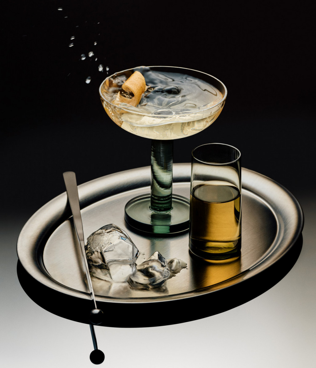 Elegant coupe glass cocktail with lemon twist garnish, served on a silver tray with ice and a mixing spoon against black backdrop.
