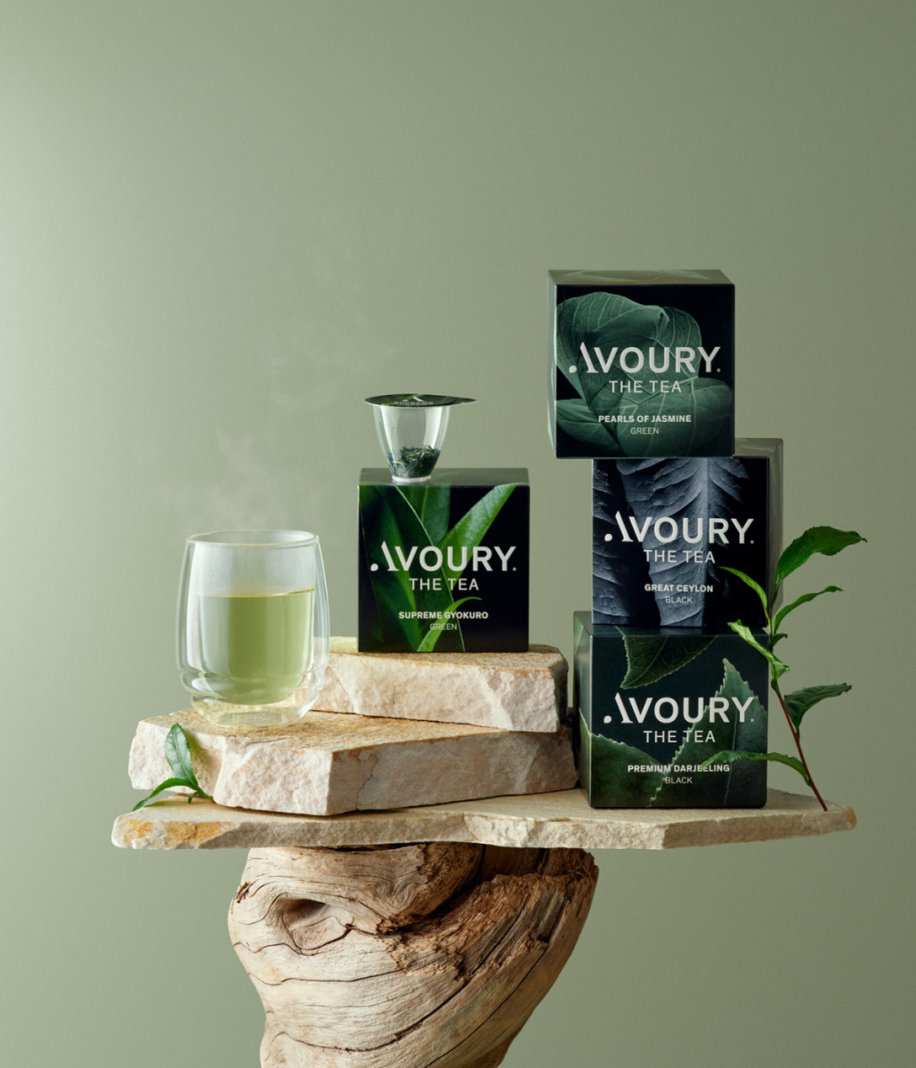 Aesthetic tea product photo featuring Avoury tea boxes, a glass of green tea, and a tea steeper arranged on travertine stones and wood.