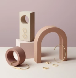 Minimalist product still life featuring gold rings and bangles arranged among geometric pastel props