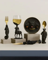 Surreal tableware set with black mythological sculpted figures supporting a gold fork, wine glass, plate, knife, and spoon.