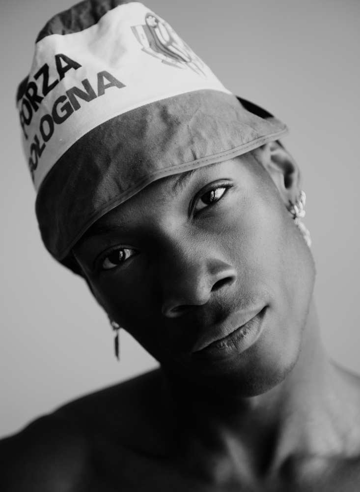 Close-up portrait of a young adult man wearing a bucket hat with the words FORZA BOLOGNA in black and white, facing forward.