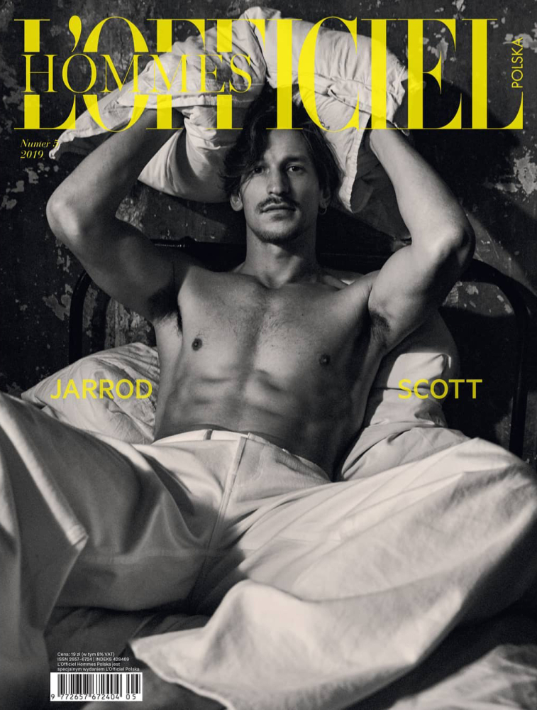 Black and white magazine cover featuring a shirtless man with a mustache, holding a pillow above his head while in bed.