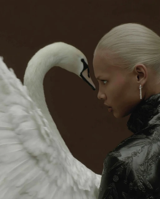 Elegant close-up of a platinum-blonde woman in profile facing a large white swan with black beak against a dark brown backdrop.