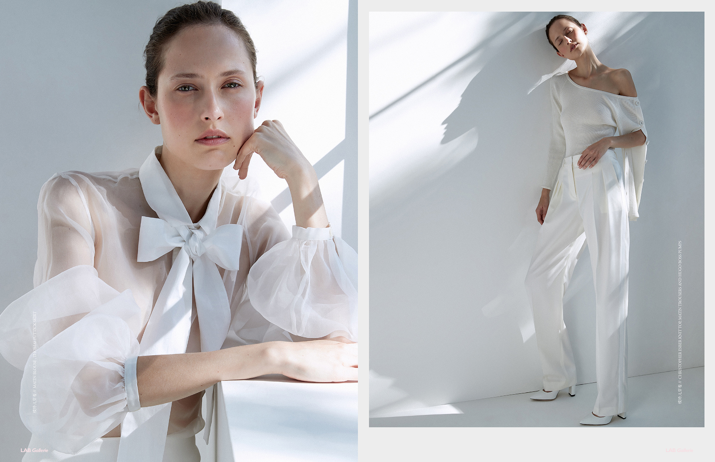 Fashion shot of a woman in a white top with a large bow and white trousers leaning against a white wall in a light, bright studio.
