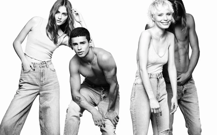 Black and white portrait of four models posing in denim jeans against a solid white background.