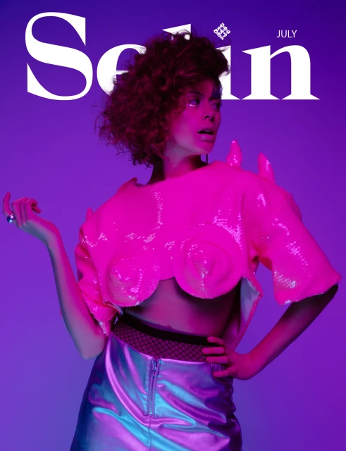 Magazine cover with a woman wearing a pink sequined top and a silver skirt against a purple background, with the title "Scén" July.