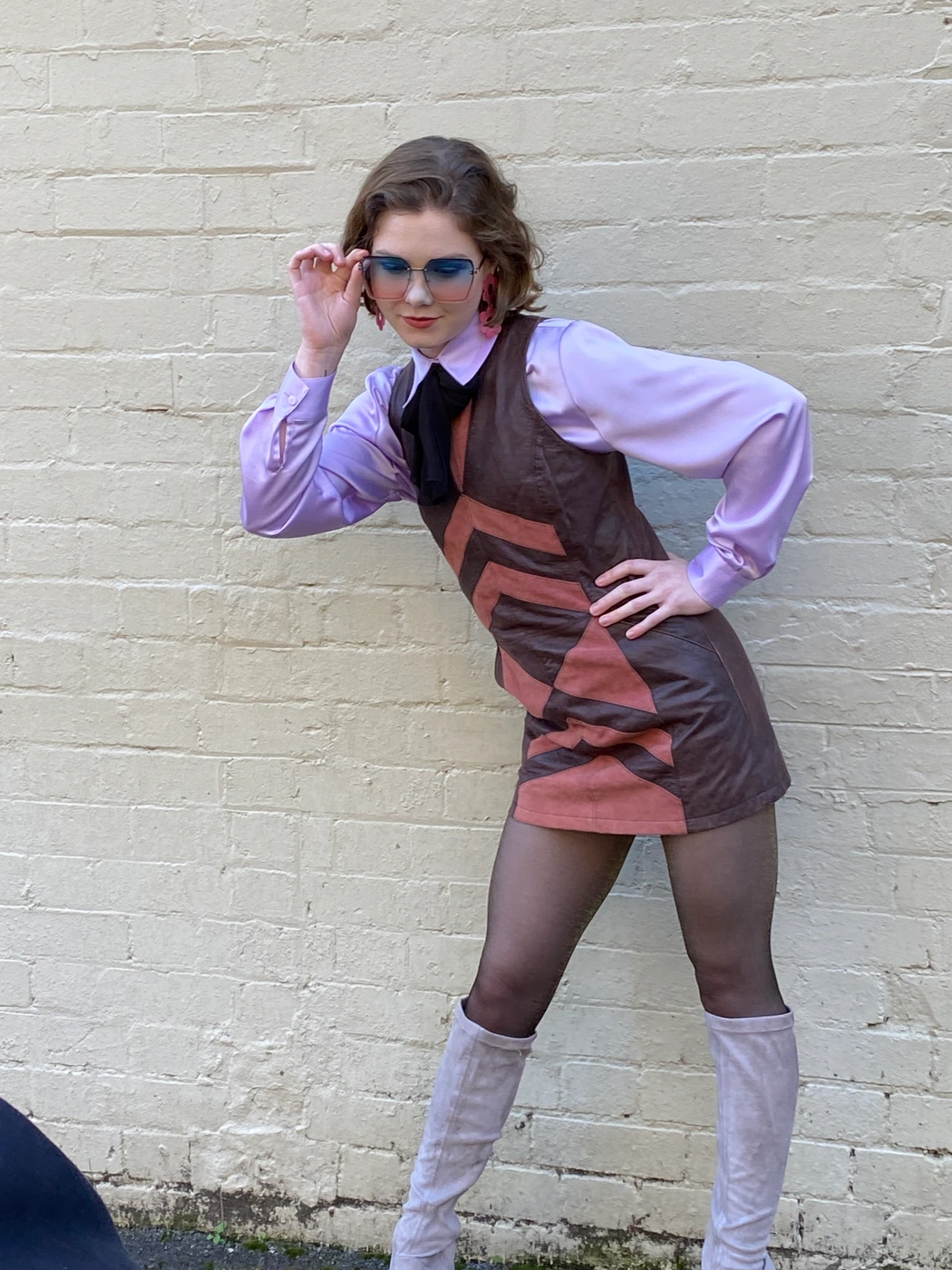Woman in retro dress and tinted sunglasses posing against a painted brick wall, styled by AM/PM Styling Solutions by Jean Brook.