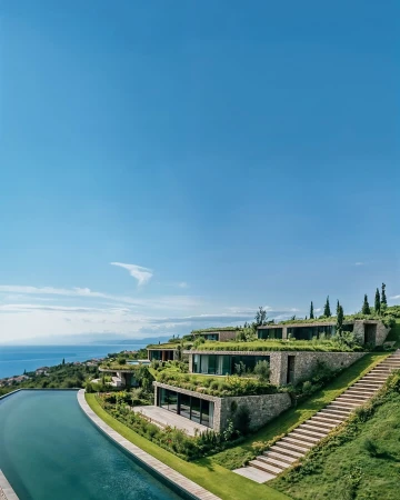 Modern hillside homes with green roofs and an infinity pool overlooking the sea on a sunny day with a clear blue sky overhead.
