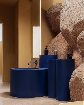 Unique bathroom design showcasing a blue cylindrical sink, cylindrical stands, and textured rock formations against a warm-toned wall.