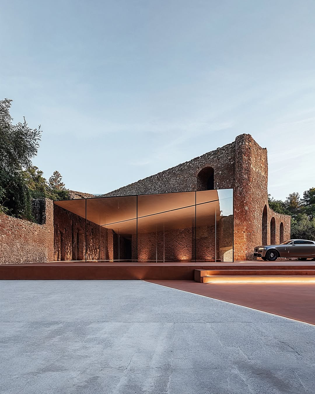 Modern architecture featuring a stone building with a contemporary glass addition, enhanced by soft lighting and a classic car.