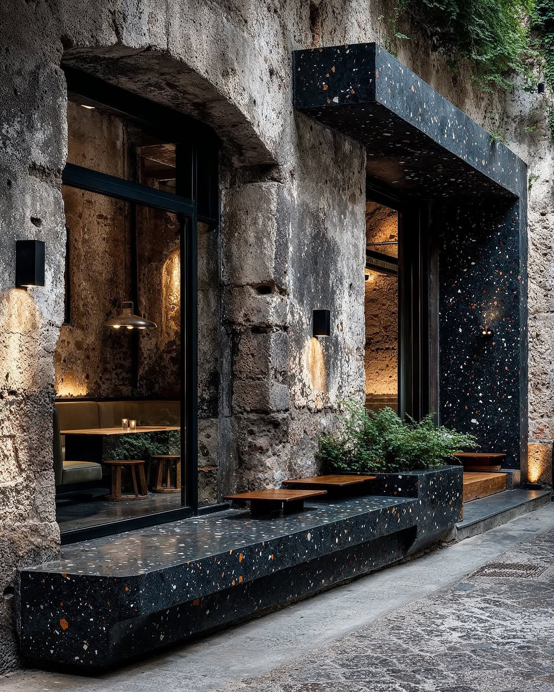 Exterior of a stone building with black terrazzo accents, including a bench, walls, and architectural features, showcasing modern design.