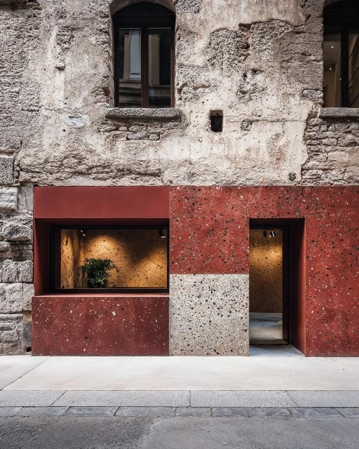 Storefront exterior featuring rust-colored speckled tiles, gray concrete sidewalk, and architectural details of an old building.
