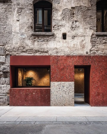 Storefront exterior featuring rust-colored speckled tiles, gray concrete sidewalk, and architectural details of an old building.