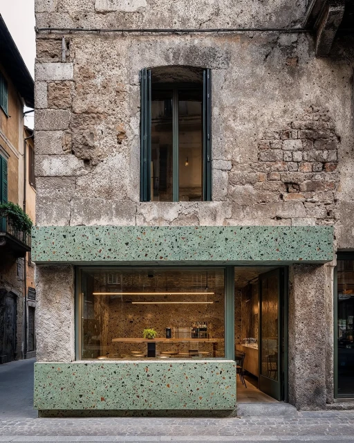 Exterior of a commercial building with a green terrazzo facade, large storefront window, and stone textured upper facade.