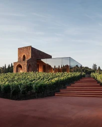 Modern mirrored glass building and rustic stone tower set amongst lush green vineyards under a clear sky.