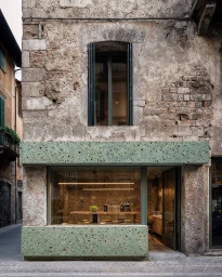 Exterior facade of a rustic stone building featuring a modern green terrazzo storefront and large display window by Dukant Atelier.