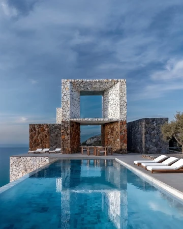 Modern stone house with infinity pool overlooking the ocean on a sunny day, architectural design showcases luxury coastal living.