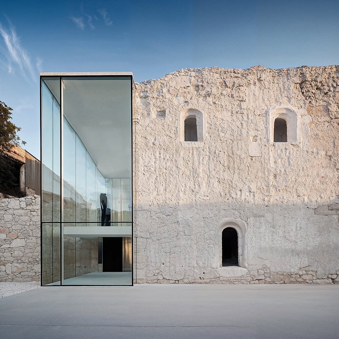 Modern glass architecture meets historic stone ruins under a blue sky, creating a captivating juxtaposition of old and new in an outdoor setting.