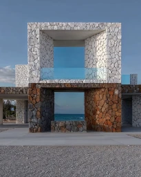 Modern stone architecture structure with square frame openings revealing the ocean and blue sky beyond.