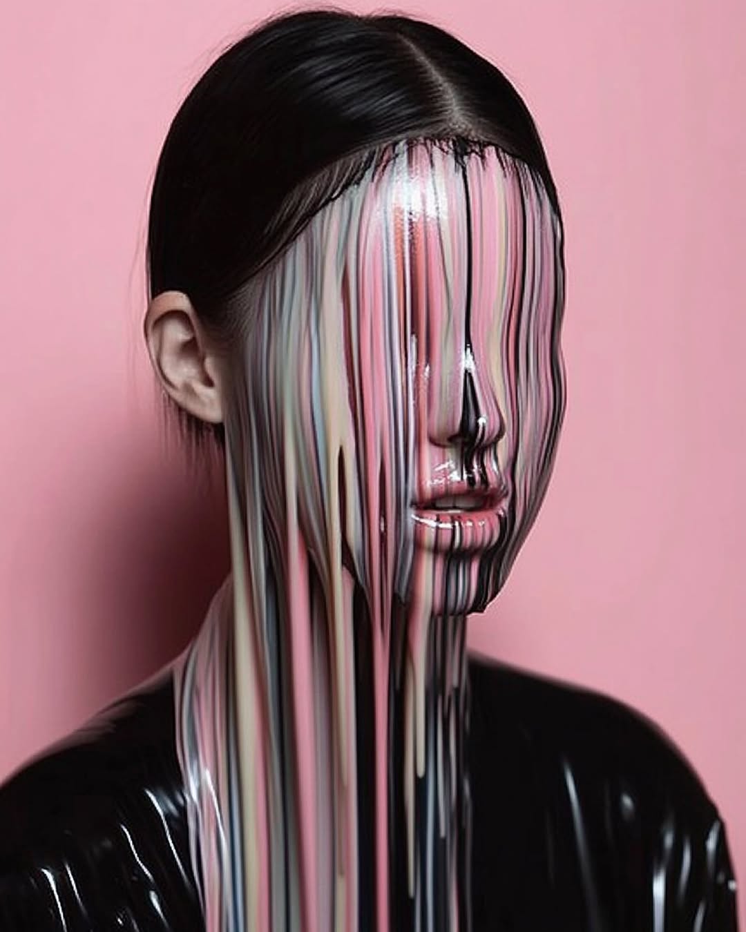 Woman with multicolored paint cascading down her face, glossy black clothing, and a solid pink background in a beauty-focused portrait.