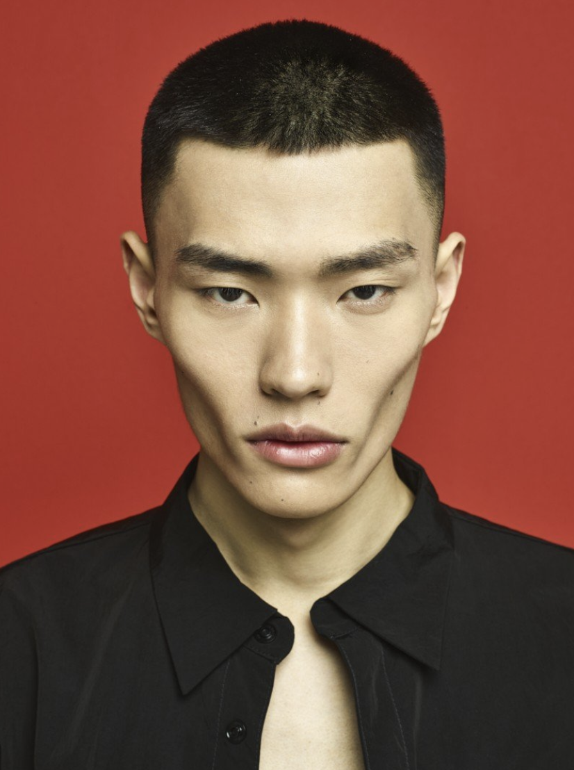 Asian man portrait with short hair against a red background, wearing a black collared shirt. Close-up headshot, studio lighting.