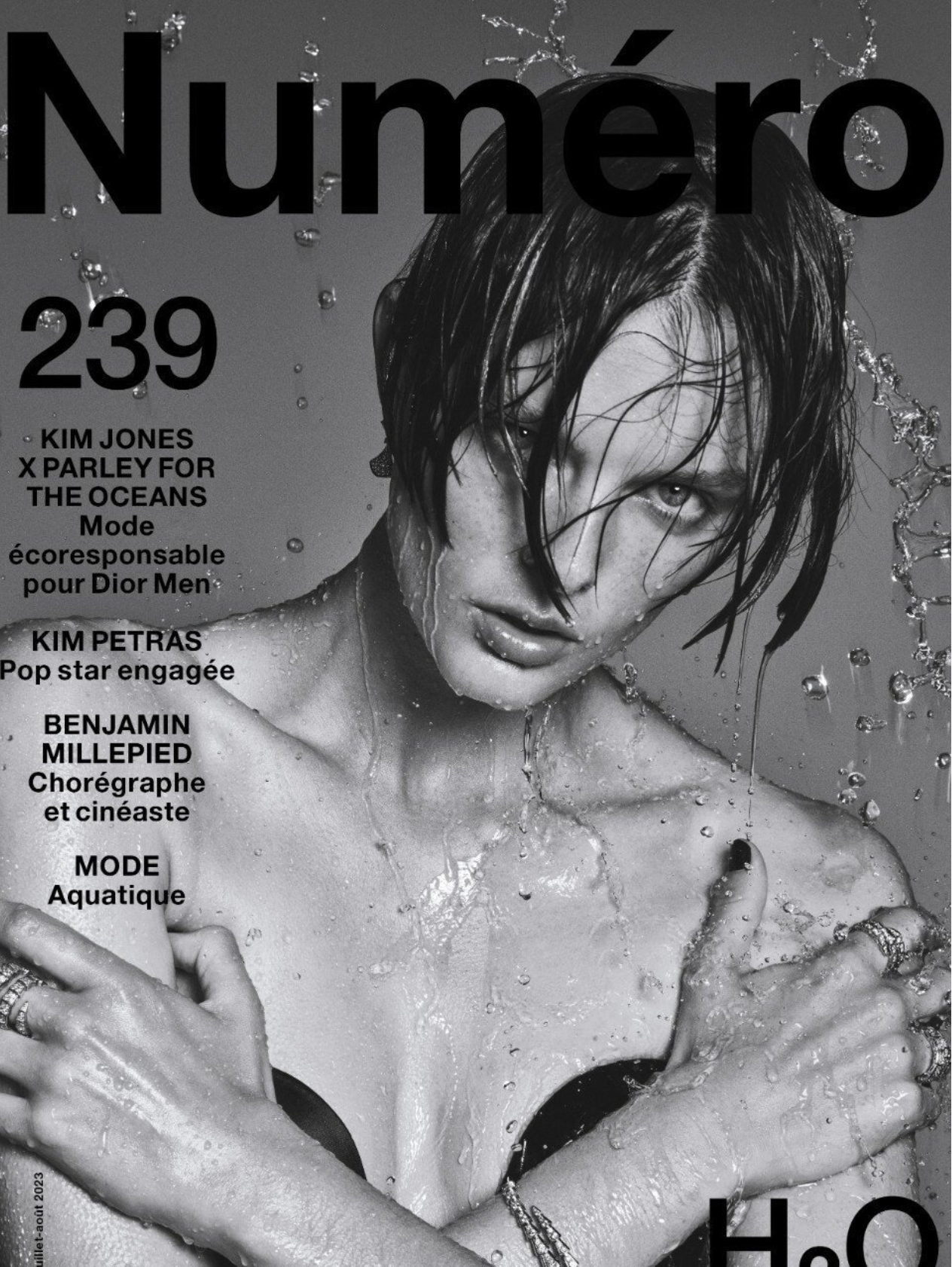 Black and white magazine cover featuring a portrait of a model with short hair, partially wet, with water droplets, wearing a black top.