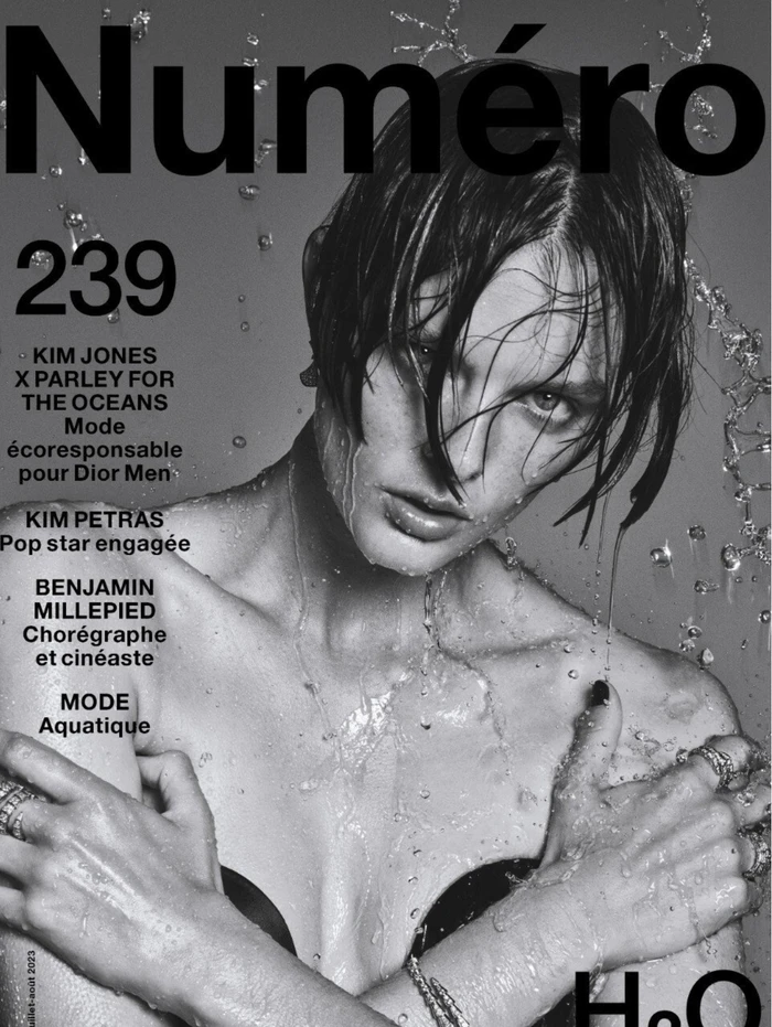 Model with wet hair and splashing water droplets on face against a grey background for Numero magazine