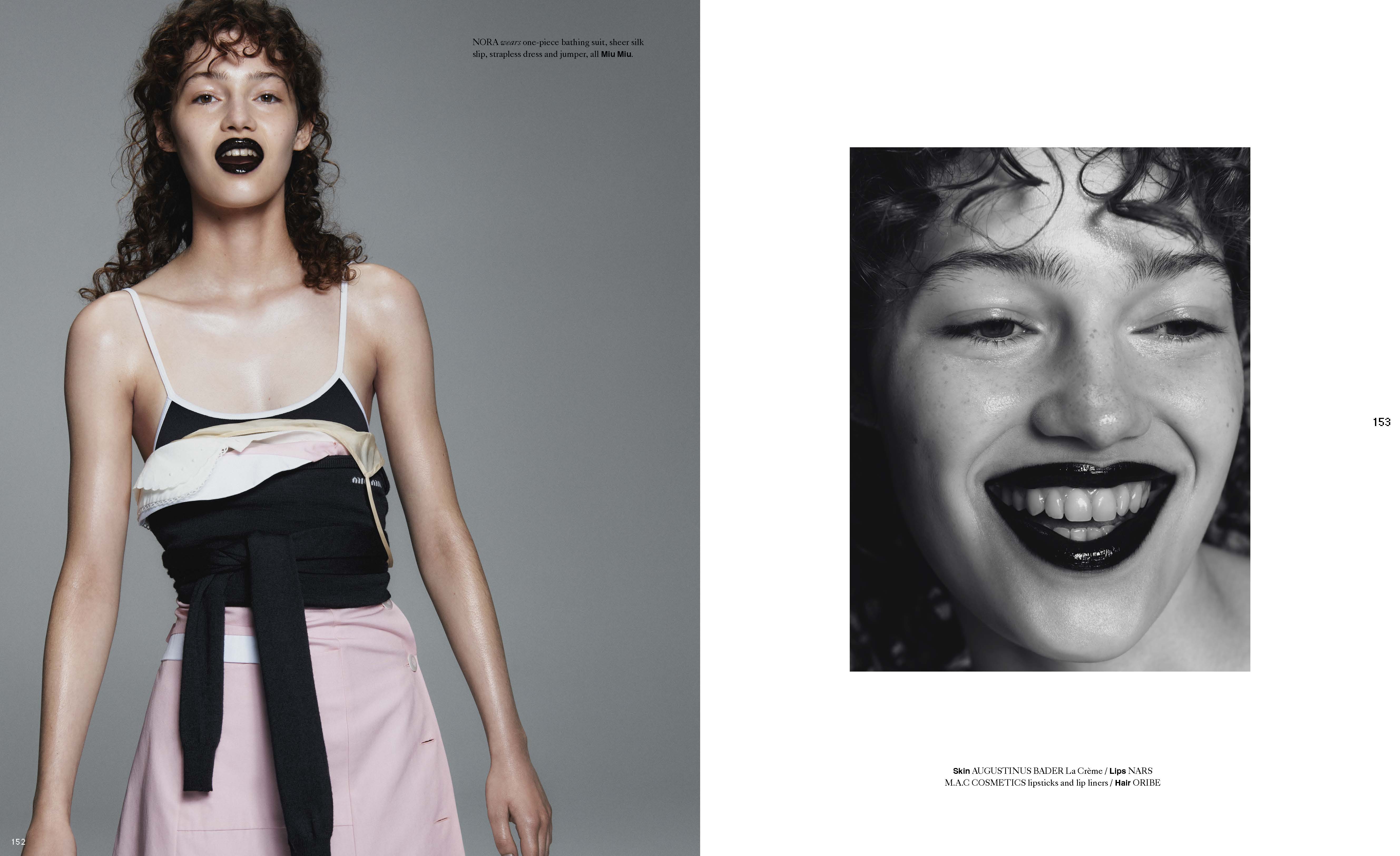 Fashion editorial shot of a model with dark lipstick wearing a tiered top and pink skirt against a grey studio backdrop.