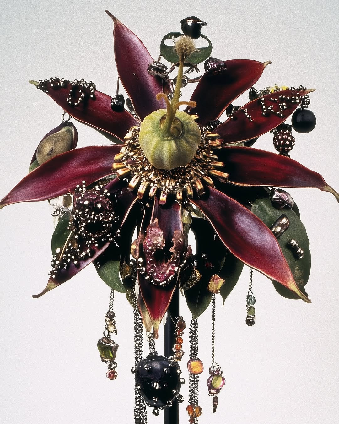 Ornamental flower sculpture with burgundy petals, gold accents, and hanging beaded chains, presented against a plain studio backdrop.