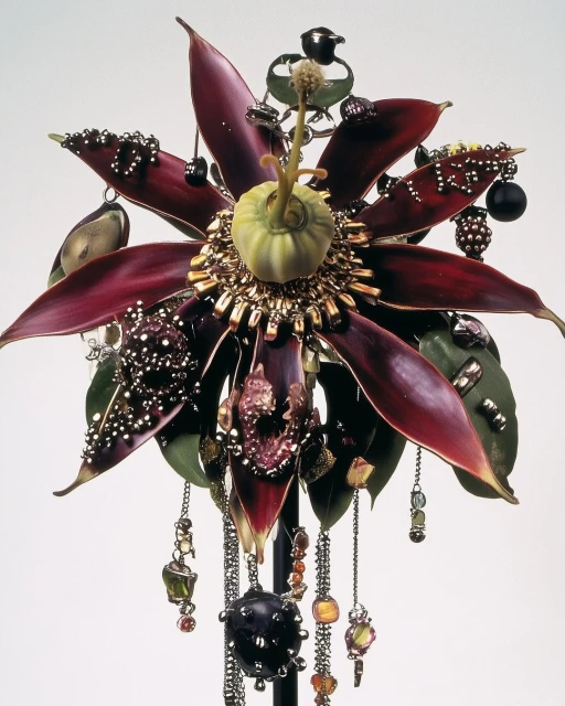 Ornamental flower sculpture with burgundy petals, gold accents, and hanging beaded chains, presented against a plain studio backdrop.
