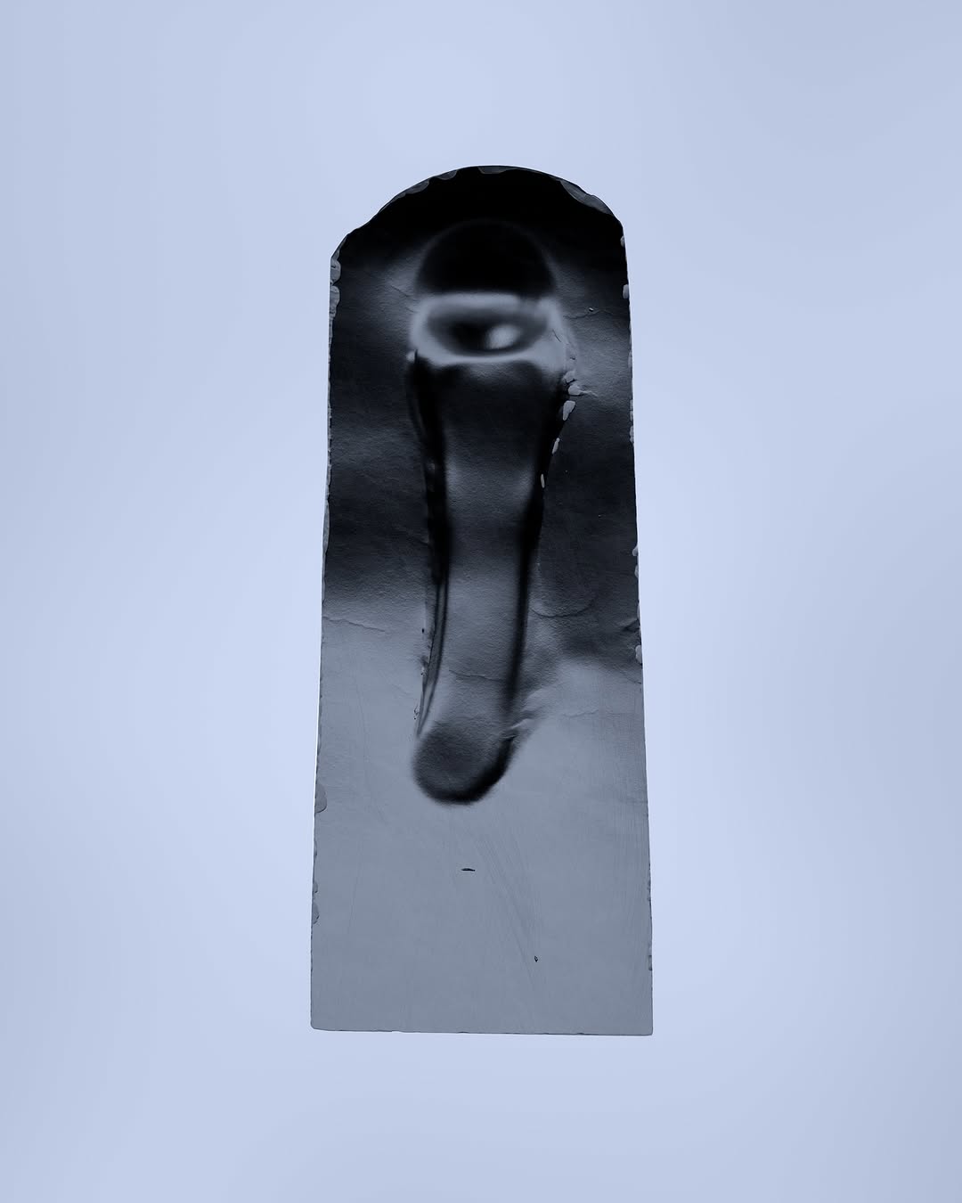 Abstract photograph of a solid, black, rectangular sculpture with an arched top against a plain, light grey background.