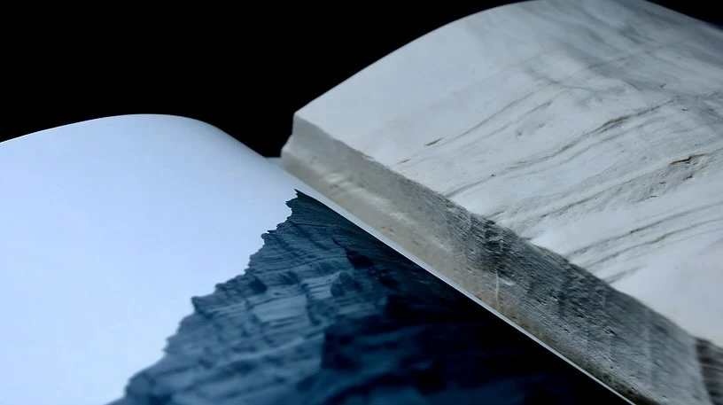 Open book displaying a landscape photograph featuring cliffs and textured pages. The photograph is set against a dark background.