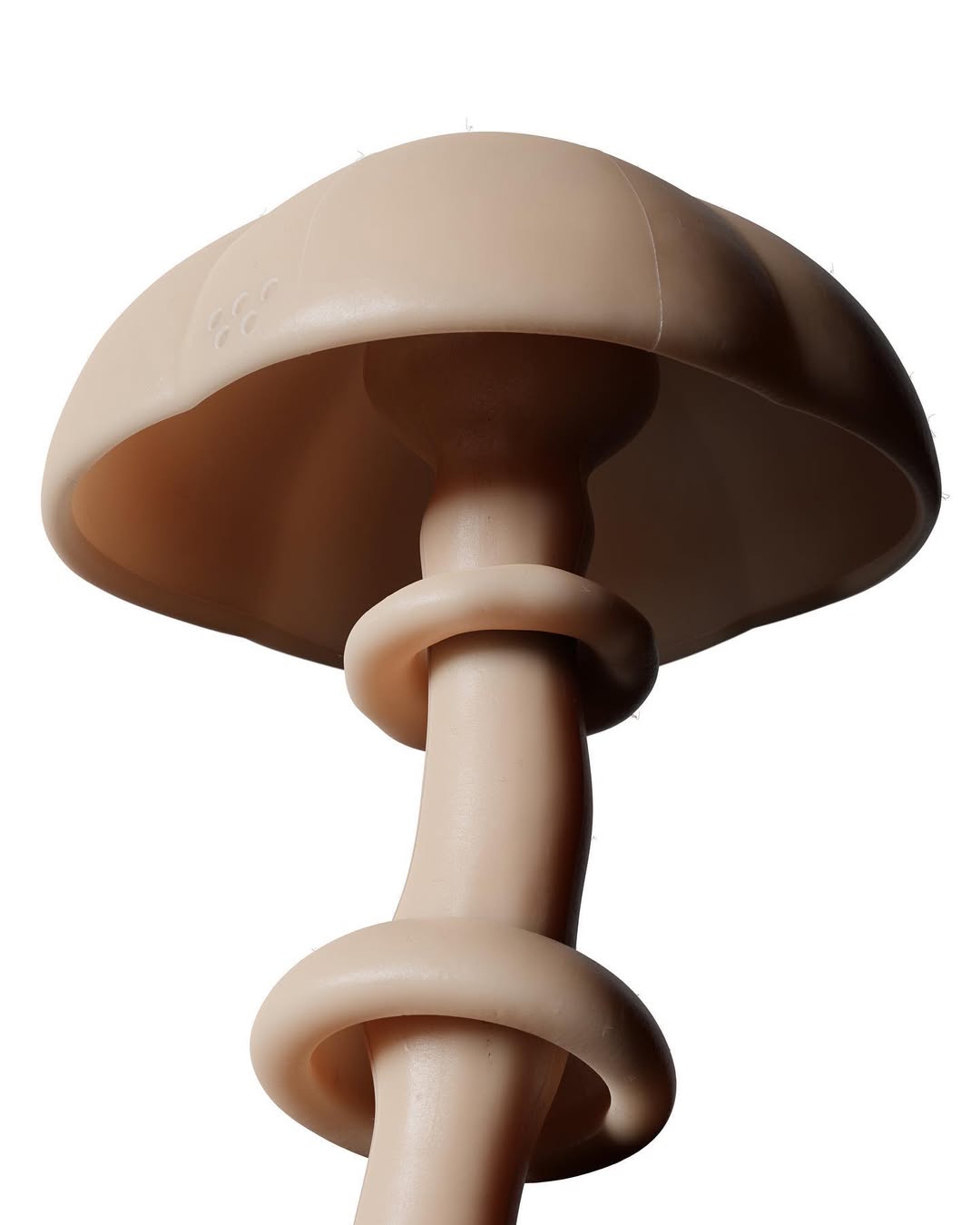 Low-angle, close-up studio shot of a mushroom-shaped sculpture in a light tan color. The piece features rounded forms and smooth texture.