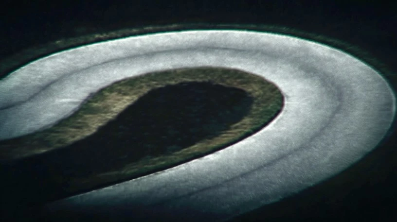 High-angle shot of an oval racetrack with white concrete barriers surrounded by dark green grass and a dark background, abstract.