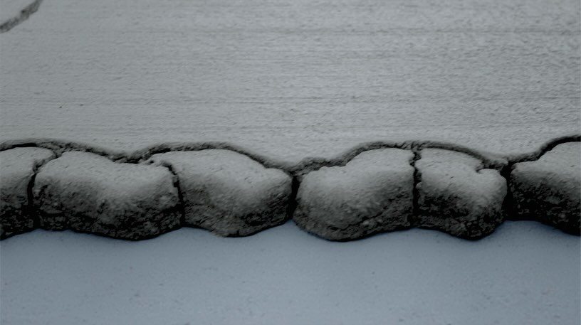 Close-up of a cracked, weathered concrete surface with an irregular textured edge, creating an abstract, monochromatic landscape.