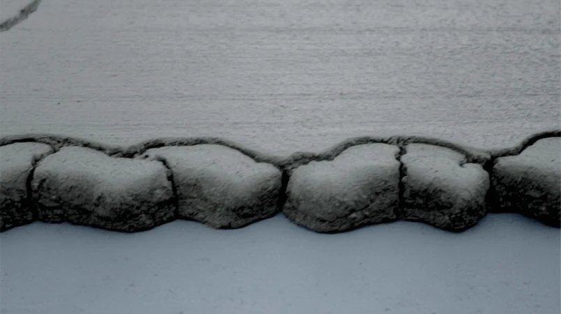 Close-up of a cracked, weathered concrete surface with an irregular textured edge, creating an abstract, monochromatic landscape.