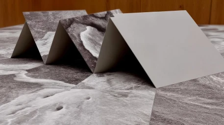 Folded paper sheet with marbled grey texture standing upright on a matching marbled surface by Arno Machado