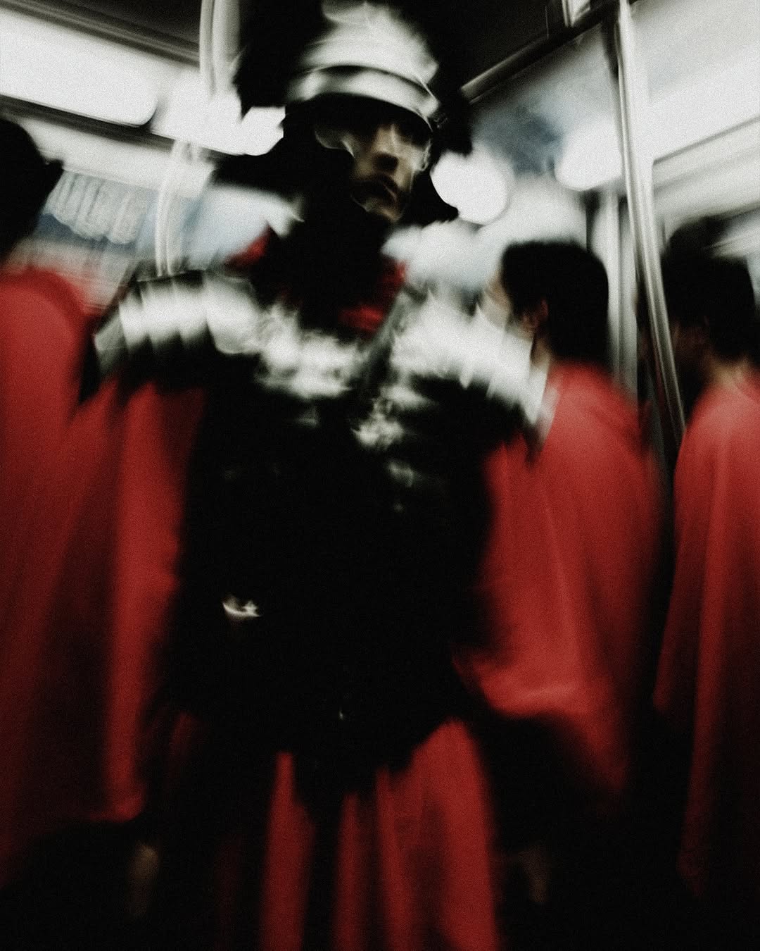 Abstract photo of a person in Roman soldier armour riding the subway with blurry figures in red tunics in the background.