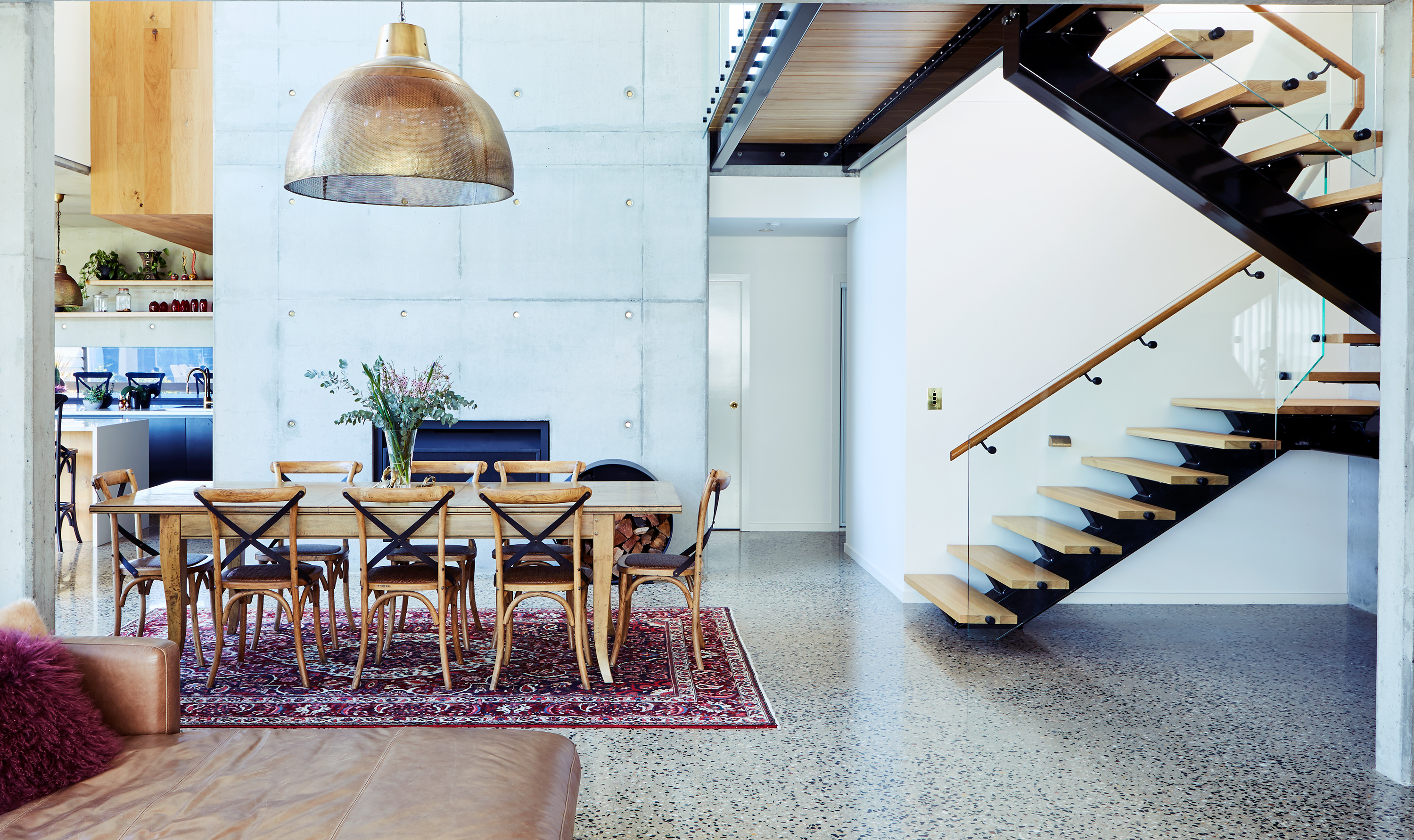 Modern interior features a dining table surrounded by chairs, a striking staircase, and a textured concrete wall providing a minimalist aesthetic.