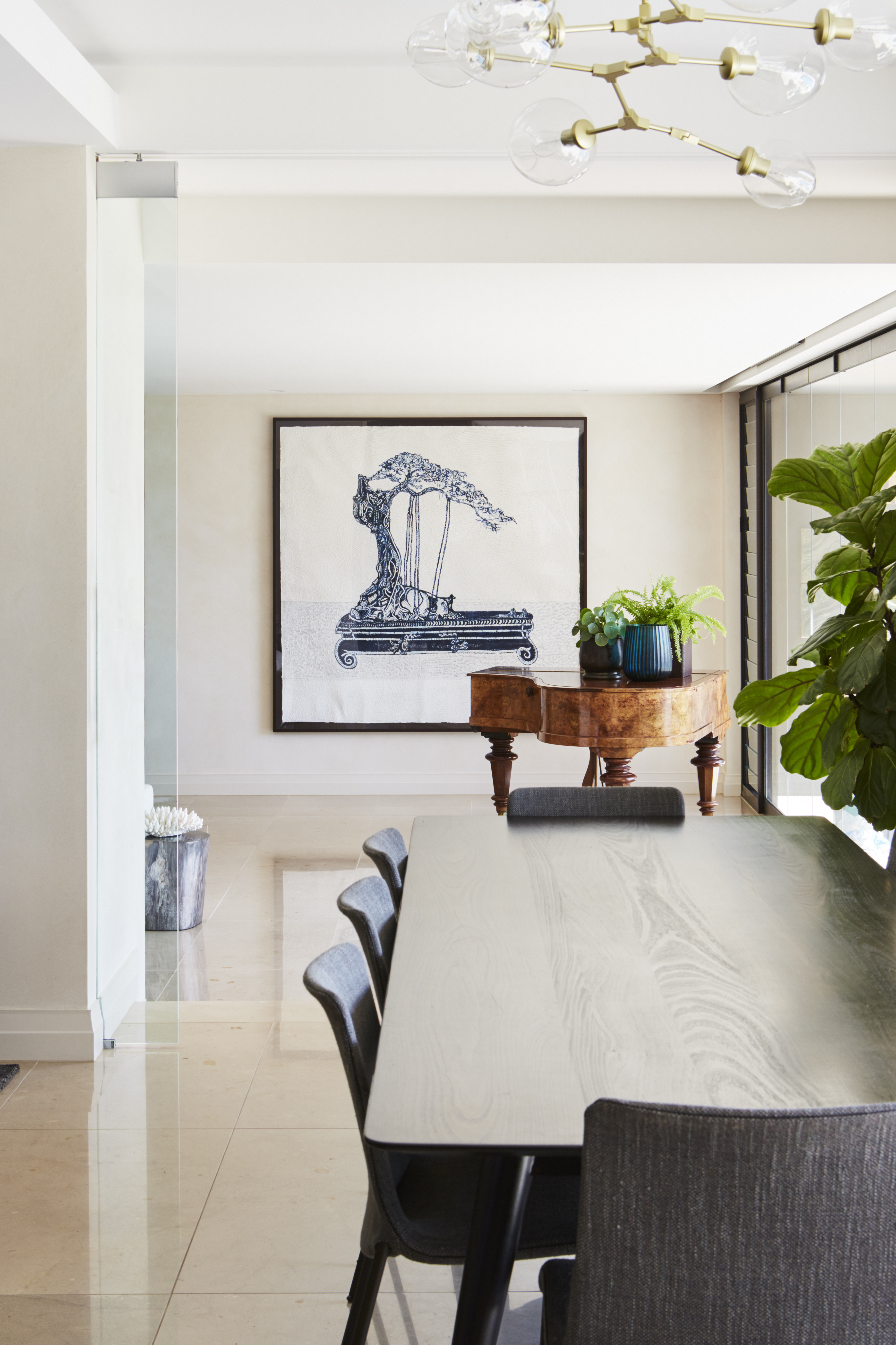 Contemporary interior featuring a dining table with chairs, a side table with plants, and an artwork in a brightly lit space.