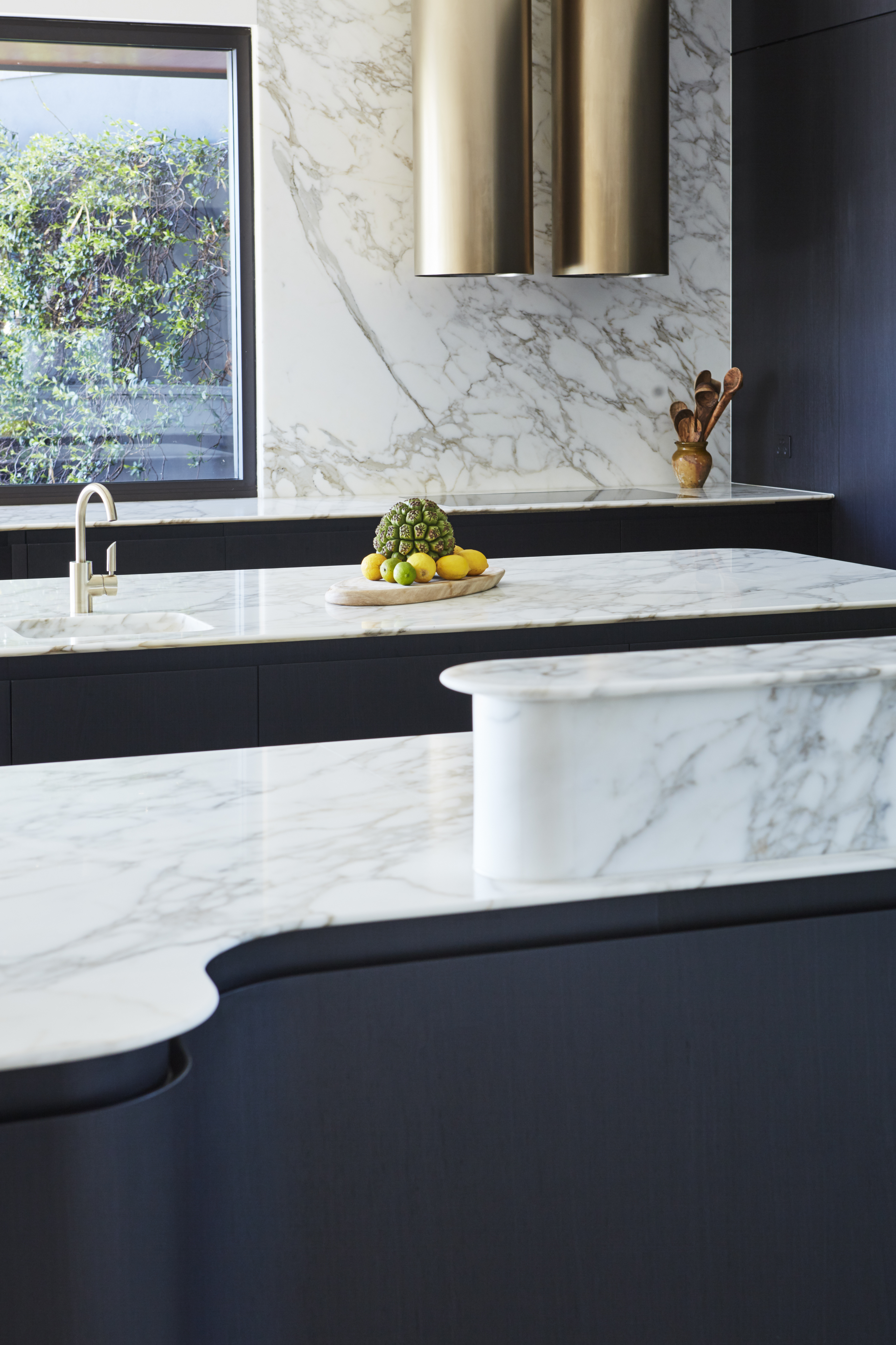 Modern kitchen interior with marble countertops, brass range hood, and a selection of fresh fruits, capturing a stylish home design.