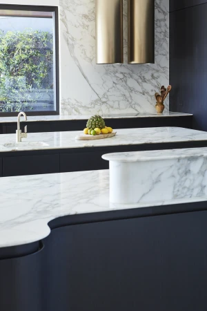 Modern kitchen interior with marble countertops, brass range hood, and a selection of fresh fruits, capturing a stylish home design.