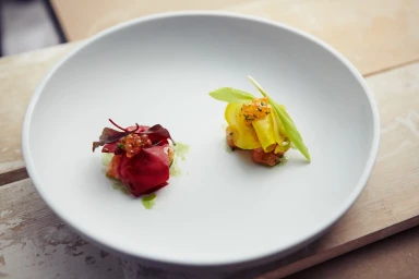 Two plated gourmet amuse-bouche dishes with red and yellow garnish in a white bowl by Leanna Maione