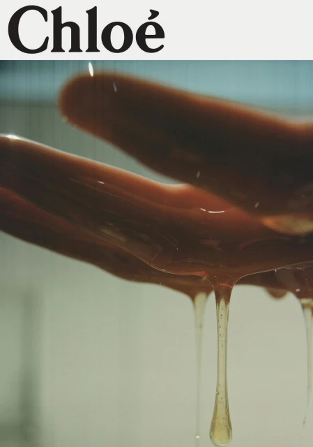 Close-up of a hand with viscous liquid dripping down, conveying a sense of richness and texture, set against a minimalist backdrop.